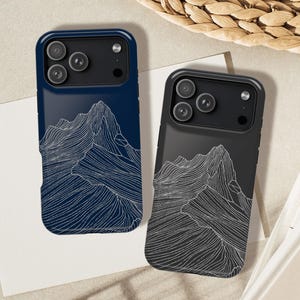 May include: Two phone cases, one navy blue and one black, each featuring a white line art mountain range design. The cases have a glossy finish and a camera bump. The cases are displayed on a neutral surface.