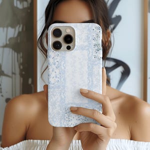 Puede incluir: Funda de teléfono con estampado floral blanco y azul claro. La funda presenta un delicado diseño floral repetitivo con un borde azul claro. La funda está diseñada para un teléfono inteligente con múltiples lentes de cámara.