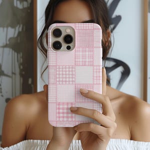 May include: A pink and white patchwork phone case. The case features a variety of plaid and gingham patterns in shades of pink and white. The phone case has a camera cutout and button placements.