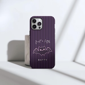 May include: A purple phone case with vertical pinstripes and a cute bat illustration. The case features the text "just a little" above the bat and the word "BATTY" below it. The case has a glossy finish.