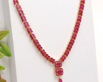 May include: A gold-toned necklace and earring set featuring ruby-colored gemstones. The necklace has a central pendant with two square stones and a teardrop-shaped stone. The earrings have a similar design, with a square stone and a teardrop.