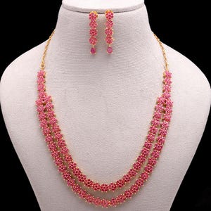 May include: A two-strand necklace and matching earrings set. The jewellery features a floral design with pink gemstones set in a gold-coloured metal. The necklace is displayed on a white mannequin.