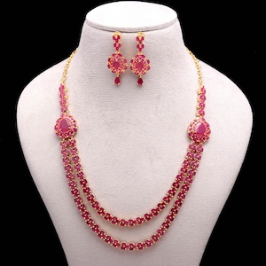 May include: A gold necklace and earring set. The necklace has two strands of small, oval ruby-coloured stones. Large ruby-coloured stones are set in the centre of the necklace. The earrings have a matching design with ruby-coloured stones.