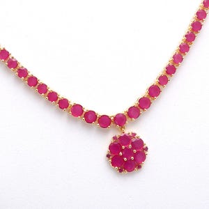 Könnte beinhalten: Eine goldfarbene Halskette mit einer Reihe von runden, leuchtend rosa Edelsteinen. Die Halskette hat einen floralen Anhänger in der Mitte, ebenfalls aus rosa Edelsteinen. Die Edelsteine sind in einem goldfarbenen Metall gefasst.