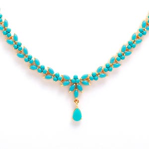May include: A gold-toned necklace with turquoise-colored stones. The necklace features a floral design with a teardrop pendant. The necklace is set against a white background.