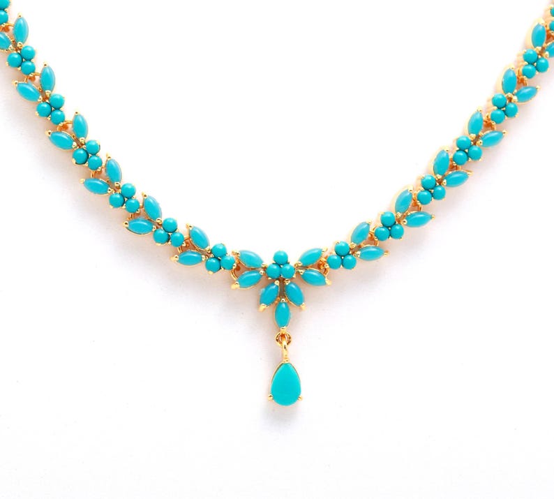 May include: A gold-toned necklace featuring turquoise-colored stones. The necklace has a floral design with a central pendant. The turquoise stones are arranged in a leaf-like pattern, creating an elegant and eye-catching piece of jewelry.