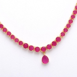 Könnte beinhalten: Eine goldfarbene Halskette mit einer Reihe runder, magentafarbener Edelsteine. Ein tropfenförmiger, magentafarbener Anhänger hängt in der Mitte. Die Halskette ist vor einem weißen Hintergrund platziert.