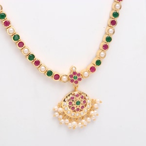 Puede incluir: Un collar dorado con un colgante y cadena a juego. La cadena presenta piedras preciosas rojas, verdes y blancas alternas. El colgante es un diseño circular con piedras preciosas rojas y verdes, y pequeñas perlas blancas.