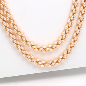 May include: Three-strand necklace featuring creamy white, teardrop-shaped beads. The beads are strung together with gold-colored metal links. The necklace is displayed on a white surface, showcasing its elegant design.