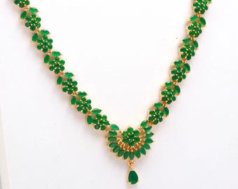 May include: A gold-toned necklace featuring a floral design with vibrant green gemstones. The necklace has a central pendant with a teardrop-shaped gemstone. The gemstones are set in a delicate, repeating pattern.