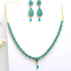 May include: A gold-toned jewelry set featuring a necklace and matching earrings. The necklace and earrings are adorned with turquoise-colored stones. The necklace has a floral design with a teardrop pendant. The earrings have a floral top and a teardrop bottom.