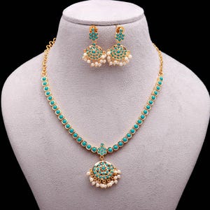 May include: A gold-toned jewelry set featuring a necklace and matching earrings. The necklace and earrings are adorned with turquoise-colored stones and small white pearls. The necklace has a pendant with a circular design. The earrings are round with a cluster of pearls.
