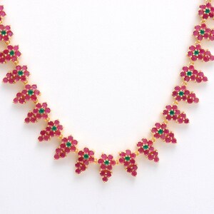 May include: A gold-toned necklace featuring clusters of pink gemstones with a central green gemstone in each cluster. The necklace is set against a white background, highlighting the vibrant colors and intricate design of the jewelry.
