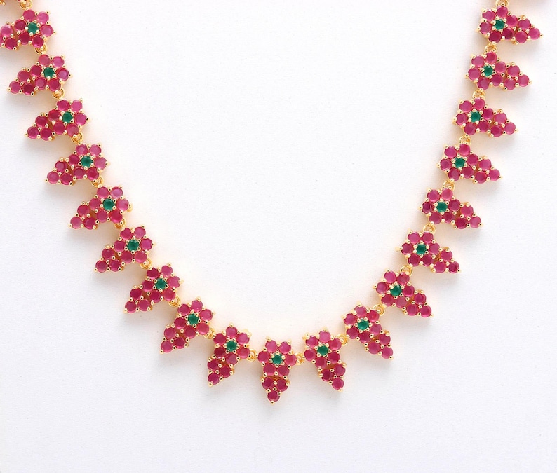 May include: A gold-toned necklace featuring clusters of pink gemstones with a central green gemstone in each cluster. The necklace is set against a white background, highlighting the vibrant colors and intricate design of the jewelry.