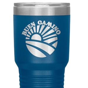 May include: A blue insulated travel mug with a silver rim and lid. The mug has the words "BUEN CAMINO" in white, and a graphic of a sun rising over a landscape. The mug is designed to keep drinks hot or cold, and is suitable for travel.