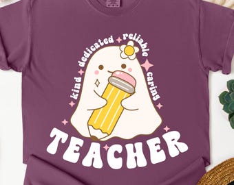 Puede incluir: Una camiseta morada con un fantasma de dibujos animados sosteniendo un lápiz. El fantasma tiene una flor y está rodeado por las palabras "kind, dedicated, reliable, caring" y la palabra "TEACHER" en blanco, fuente retro.