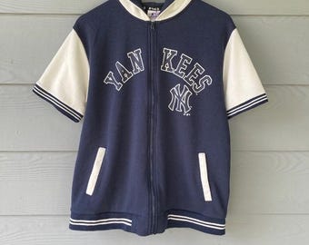 May include: Navy blue zip-up hooded sweatshirt with white short sleeves. The front features the text "YANKEES" and "NY" logo in white. The sleeves have a white stripe detail. The sweatshirt has two front pockets and a white hood lining.