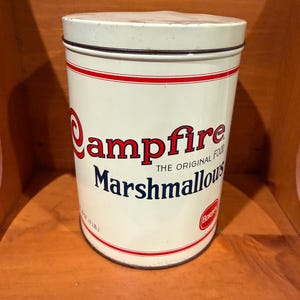 May include: A cylindrical off-white metal tin with a lid, featuring red and blue text that reads Campfire Marshmallows, The Original Food, and Borden. The container includes red horizontal stripes and a net weight label of 16 oz (1 lb).