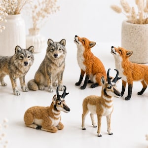 May include: A collection of six needle-felted animal figurines including two gray wolves, two orange foxes with black legs, and two brown and white pronghorn antelopes. The figures are arranged in a group, with some standing and some sitting.