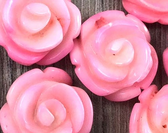 May include: Close-up of pink coral rose beads. The beads are carved in the shape of roses and have a smooth, polished finish.