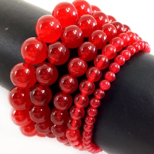 May include: A stack of red gemstone beads of varying sizes. The beads are round and have a glossy finish.