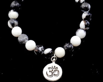 May include: A black and white beaded bracelet with a silver Om charm. The beads are round and have a marbled pattern.