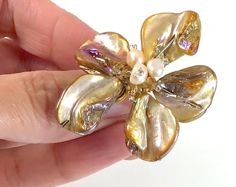 May include: A gold flower ring made of iridescent mother of pearl with white pearl accents.