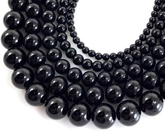 May include: Close-up of multiple strands of black, glossy beads. The beads vary in size, ranging from large, prominent spheres to smaller, delicate orbs. The arrangement suggests a necklace or jewelry design, with a focus on the reflective surfaces of the beads.