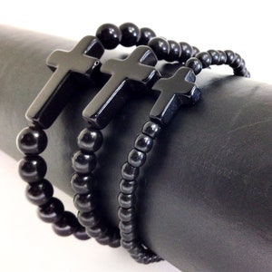 May include: Three black beaded bracelets with black cross charms. The bracelets are layered on top of each other.
