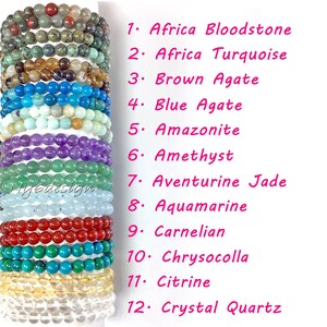 May include: Twelve stacked bracelets made of different types of gemstones, including bloodstone, turquoise, agate, amazonite, amethyst, aventurine jade, aquamarine, carnelian, chrysocolla, citrine, and crystal quartz. Each bracelet is labeled with its corresponding gemstone name.