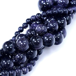 May include: A strand of dark blue gemstone beads with a sparkly, speckled finish. The beads are round and smooth, and they are strung together in a loose, flowing pattern.