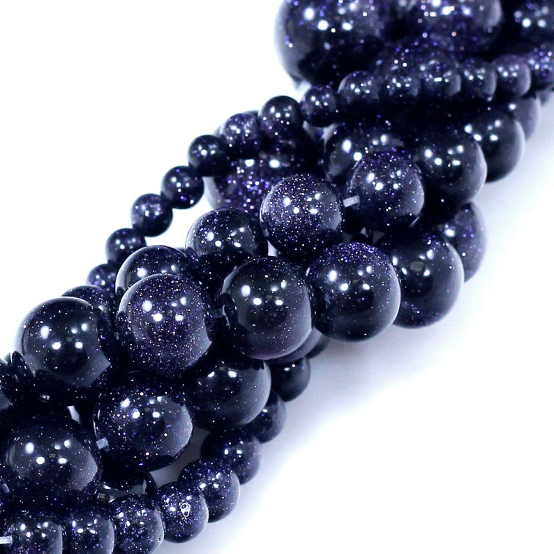 May include: A strand of dark blue gemstone beads with a sparkly, speckled finish. The beads are round and smooth, and they are strung together in a loose, flowing pattern.
