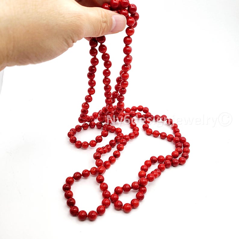 May include: A long, vibrant red beaded necklace. The necklace is composed of numerous small, round beads, creating a continuous strand. The beads are a deep, saturated red color, and the necklace is displayed against a white background.