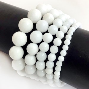 May include: A set of white gemstone bracelets with round beads of varying sizes. The bracelets are stacked on top of each other on a black surface.