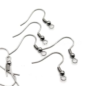 May include: Close-up of several silver-colored earring hooks. The hooks have a curved design with a coiled spring and a small ball at the end. The hooks are on a white background.