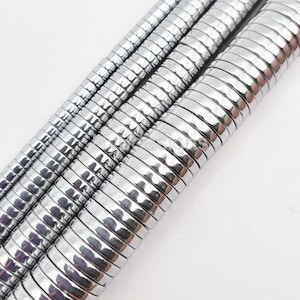 May include: A strand of silver hematite beads, each bead is round and has a hammered texture. The beads are stacked on top of each other, creating a visual pattern.
