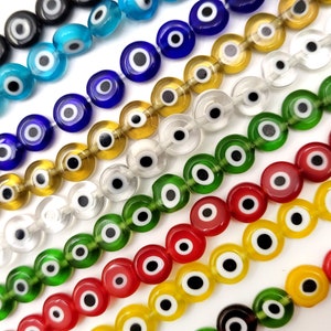 May include: Assortment of colorful glass evil eye beads with white pupils. The beads are arranged in rows, with each row featuring a different color. The colors include black, blue, yellow, clear, green, red, and yellow.