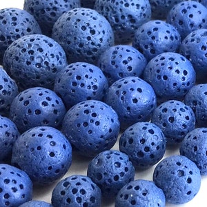 May include: A close-up of a collection of blue lava rock beads. The beads are round and have a porous surface.