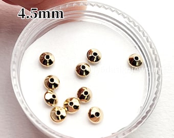 May include: A clear plastic container holding several small, gold-colored beads. The beads are round with a hole through the center. The text "4.5mm" is printed in black on the top left of the image. The beads are likely for jewelry making.