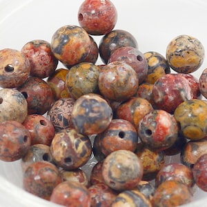 May include: A collection of round, brown, red, and white jasper beads with a mottled pattern. The beads have a hole drilled through the center for stringing.