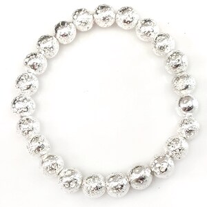 May include: A silver beaded bracelet with a textured, hammered appearance. The bracelet features multiple round beads strung together, creating a flexible and stylish accessory. The beads have a metallic sheen, reflecting light.