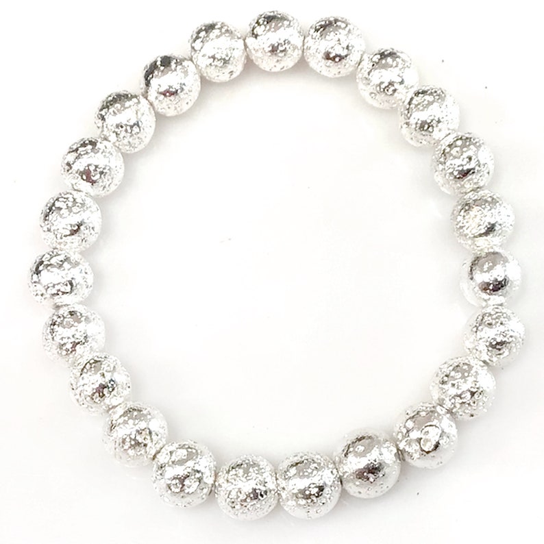 May include: A silver beaded bracelet with a textured, hammered appearance. The bracelet features multiple round beads strung together, creating a flexible and stylish accessory. The beads have a metallic sheen, reflecting light.