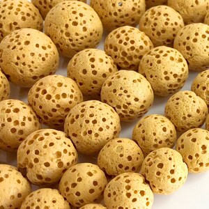 May include: A close-up of a string of light brown lava rock beads. The beads are round and have a porous texture.