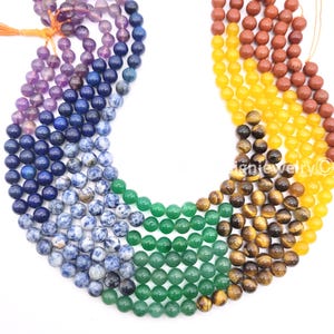 May include: A collection of colorful gemstone beads in a rainbow arrangement. The beads are round and vary in color, including purple, blue, green, yellow, and brown. The beads are strung together, ready for jewelry making.