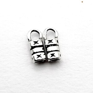 May include: Two silver-colored, cylindrical jewelry beads with a star design. Each bead has a curved top and three sections with star-shaped cutouts. The beads are displayed on a white surface.