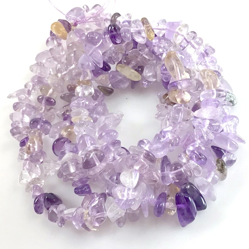 May include: A strand of amethyst chip beads in shades of purple and lavender. The beads are irregular in shape and size, with some having a more pointed or elongated shape.