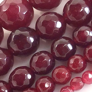 May include: A close-up of a strand of dark red gemstone beads. The beads are faceted and have a glossy finish.