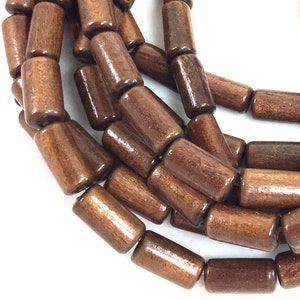 May include: Close-up of a strand of dark brown wooden beads. The beads are cylindrical with rounded ends and have a glossy finish. The beads are strung together, creating a necklace or bracelet.