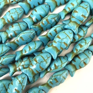 May include: Close-up of turquoise fish-shaped beads with brown veining. The beads are arranged in rows, showcasing their detailed design. These beads are ideal for jewelry making, such as necklaces and bracelets.