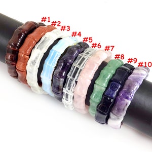 May include: Ten different colored bracelets made of natural stone beads. The bracelets are stacked on top of each other on a black surface. The bracelets are numbered 1 through 10.